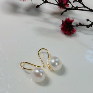 Pearl earrings with gold hooks on a white surface with pink flowers in the background